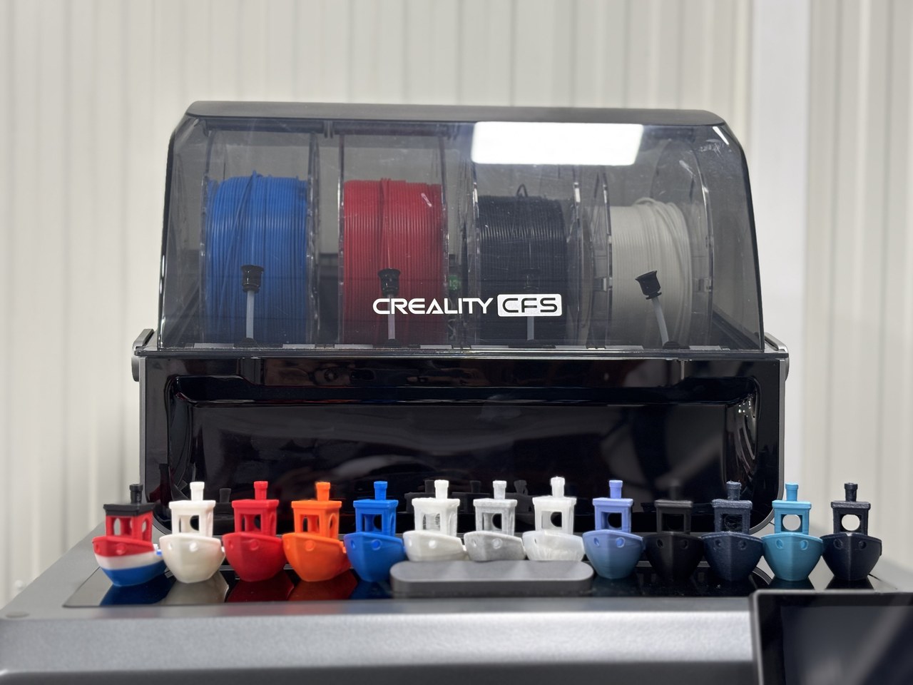 Multi-material filament system loaded with four colours beside a row of multi-coloured printed boats