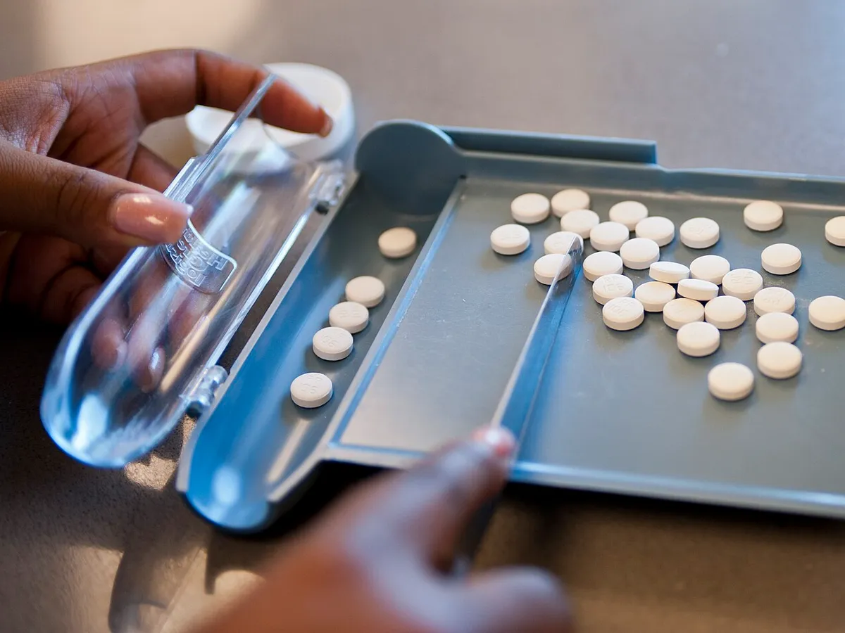 Hands counting tablets on a counting tray with a spatula
