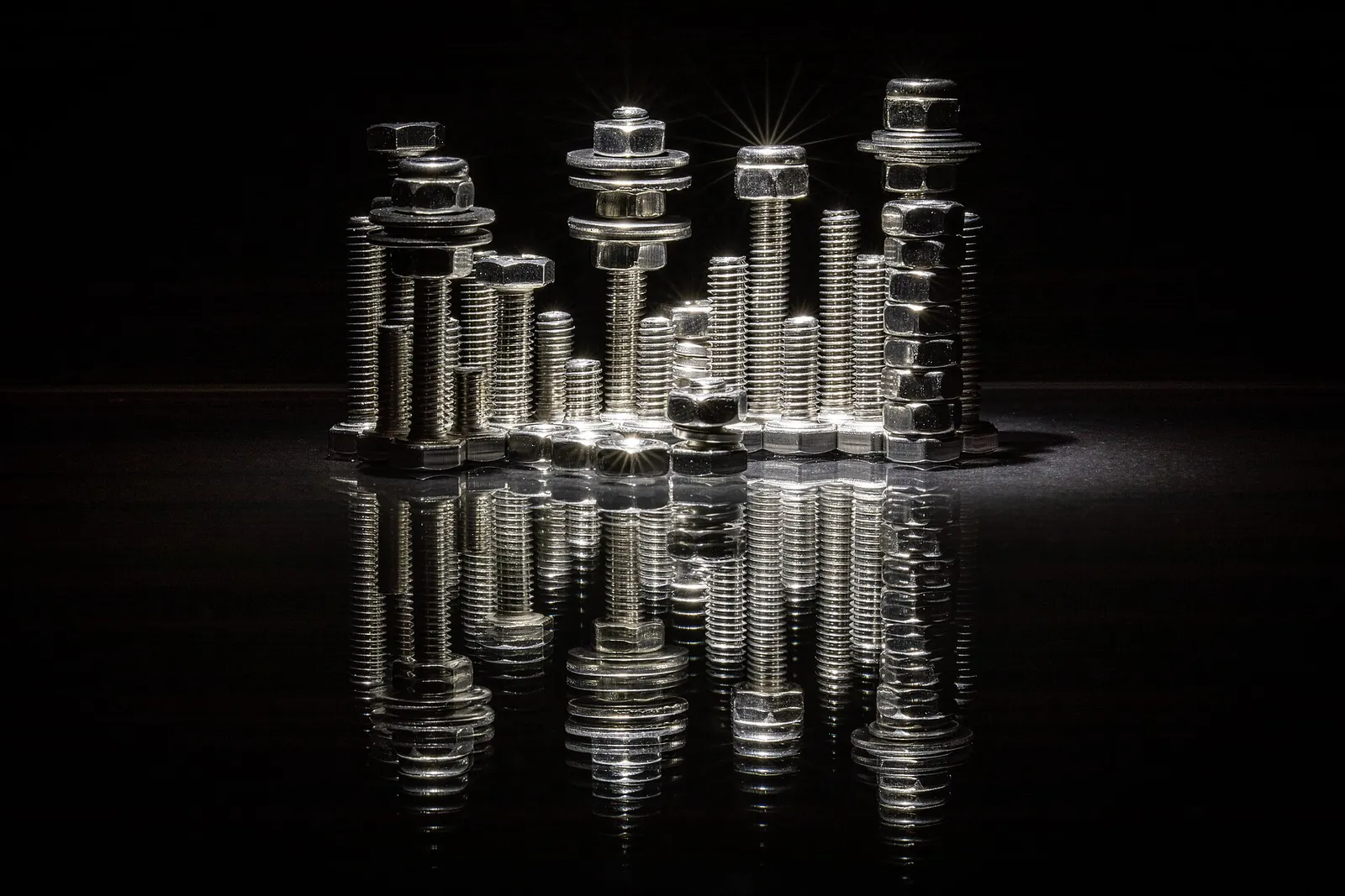Polished steel bolts, nuts and washers throwing bright specular reflections onto a mirror surface