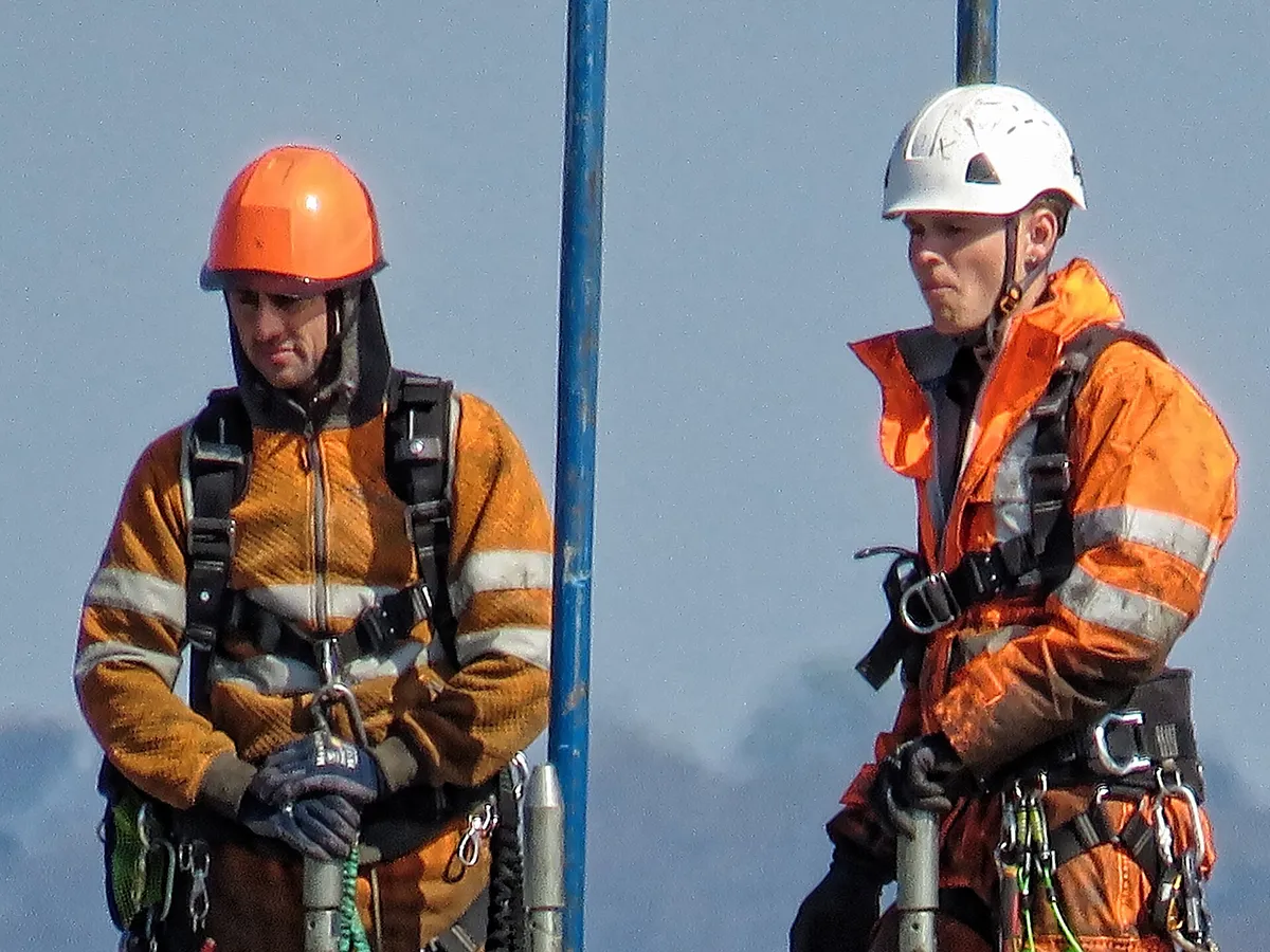 Two workers wearing hard hats, high visibility clothing and fall protection harnesses